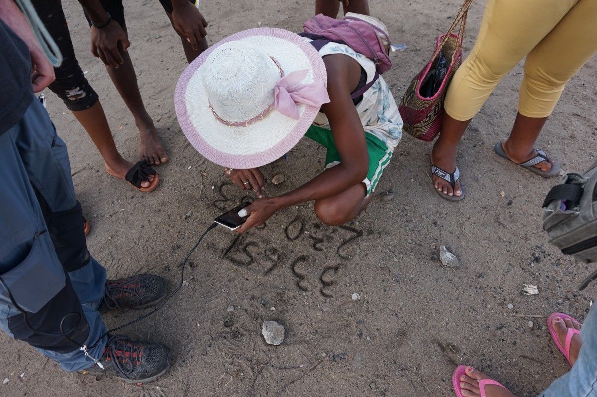 A person calls a phone number written on the sand in Madagascar after cyclone Batsirai